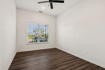 A room with a ceiling fan and a window showing a parking lot outside